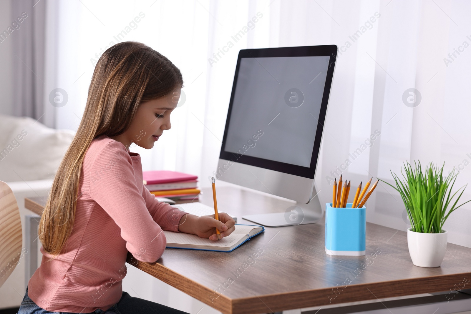 Photo of E-learning. Cute girl taking notes during online lesson at table indoors