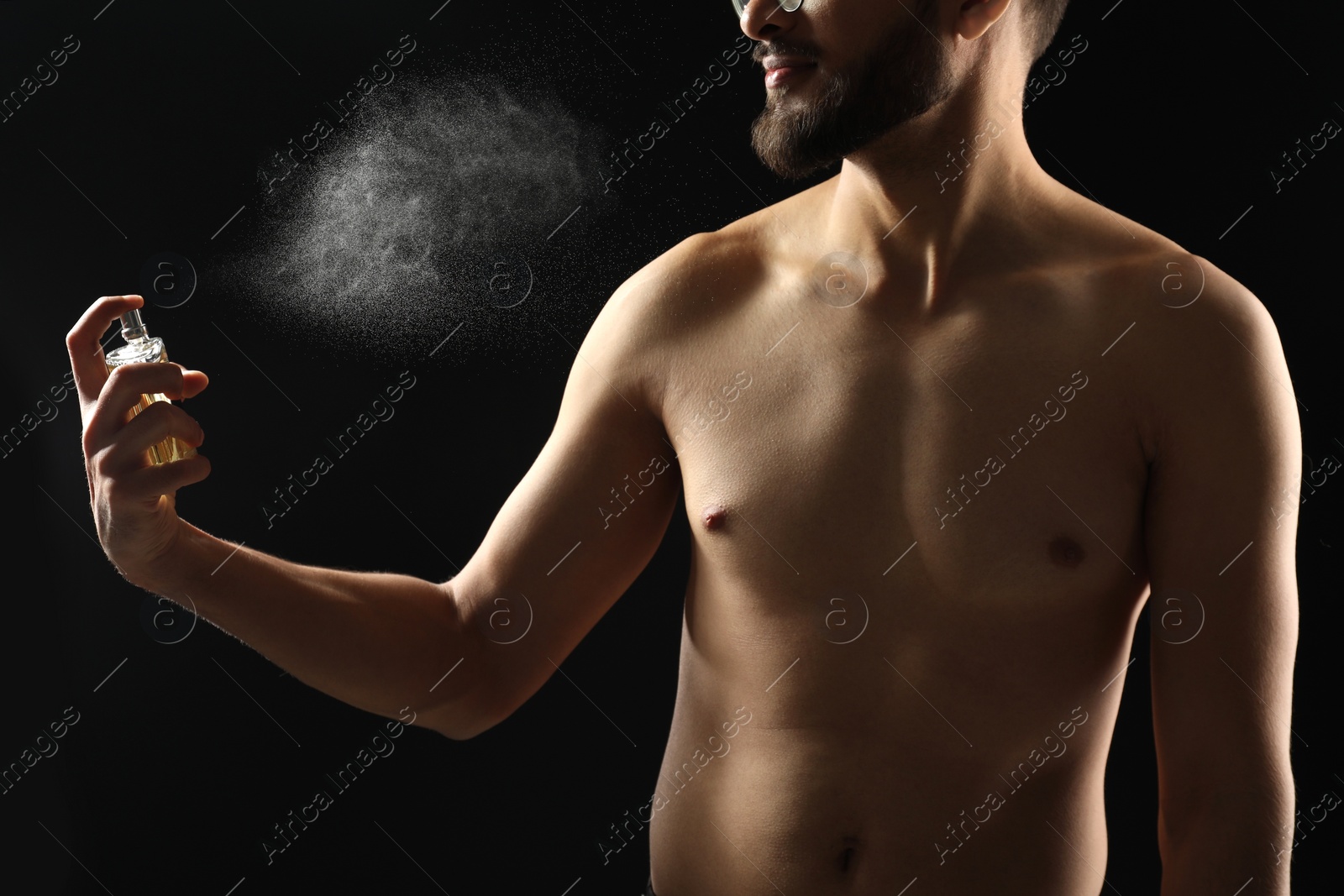 Photo of Man spraying luxury perfume on dark background, closeup