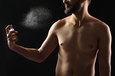 Man spraying luxury perfume on dark background, closeup