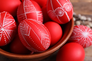 Photo of Wooden bowl with red painted Easter eggs on table, closeup