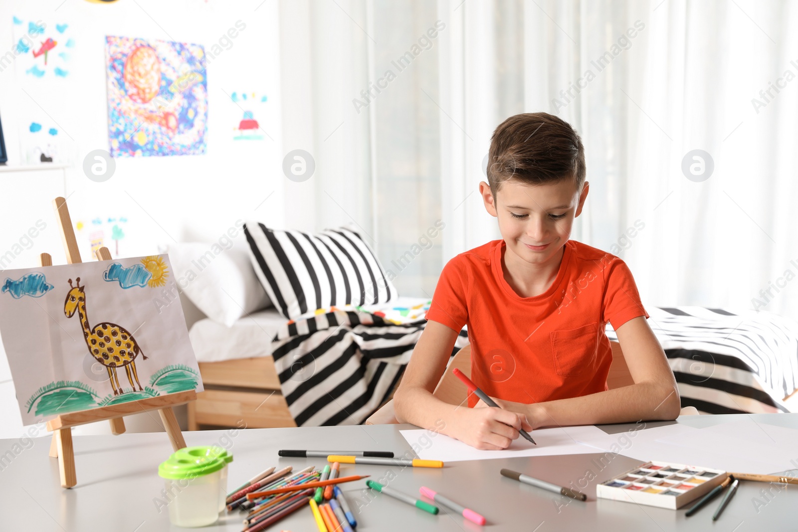 Photo of Little child drawing picture at table with painting tools indoors