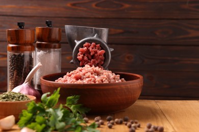 Manual meat grinder with beef mince, spices and parsley on wooden table, space for text