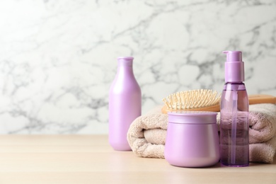 Different hair care products, towel and brush on wooden table. Space for text