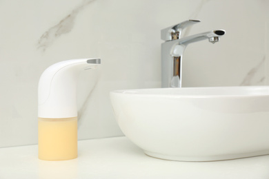 Modern automatic soap dispenser near sink in bathroom, closeup