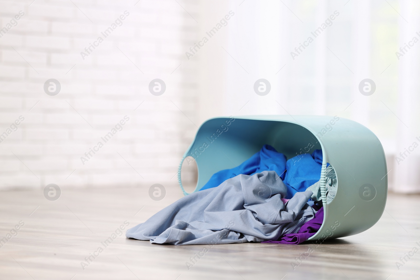 Photo of Laundry basket with scattered dirty clothes on floor in room, space for text