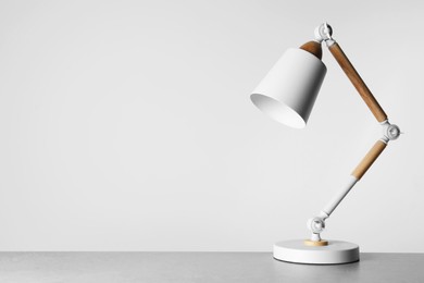 Photo of Stylish modern desk lamp on light gray table, space for text