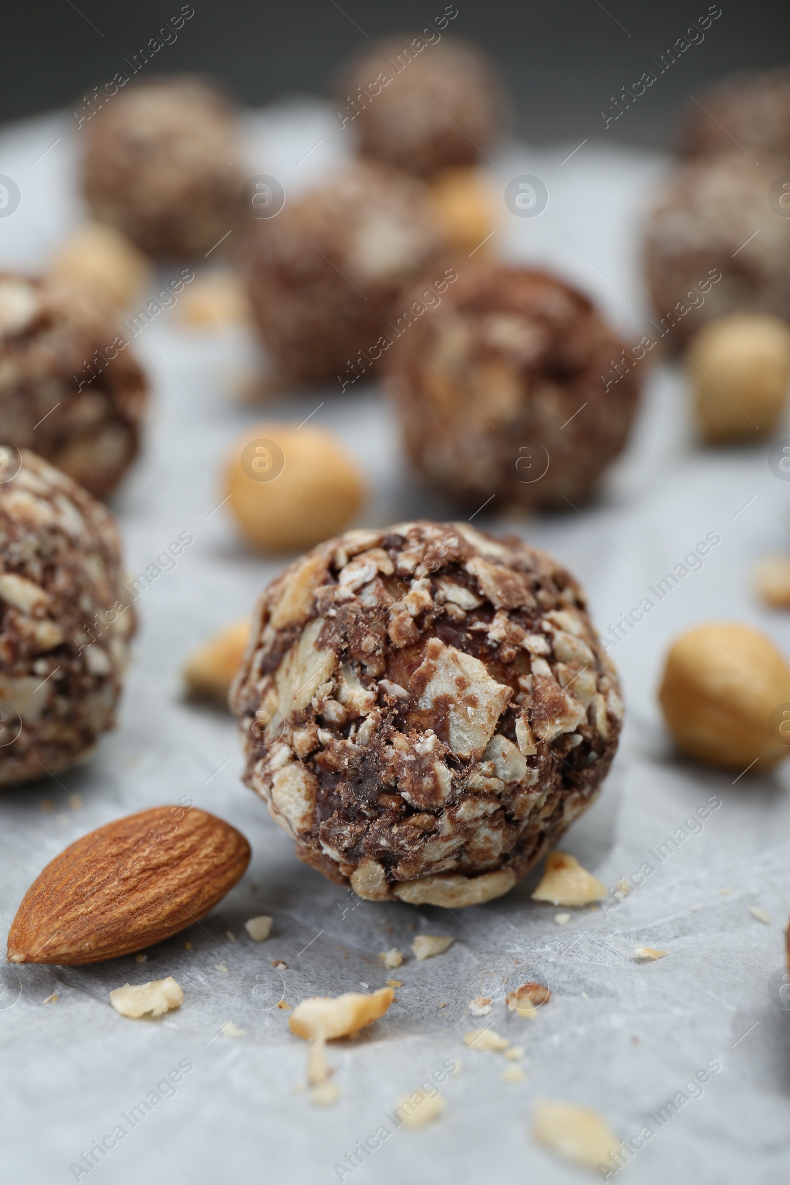 Photo of Delicious sweet chocolate candies and nuts on parchment paper, closeup