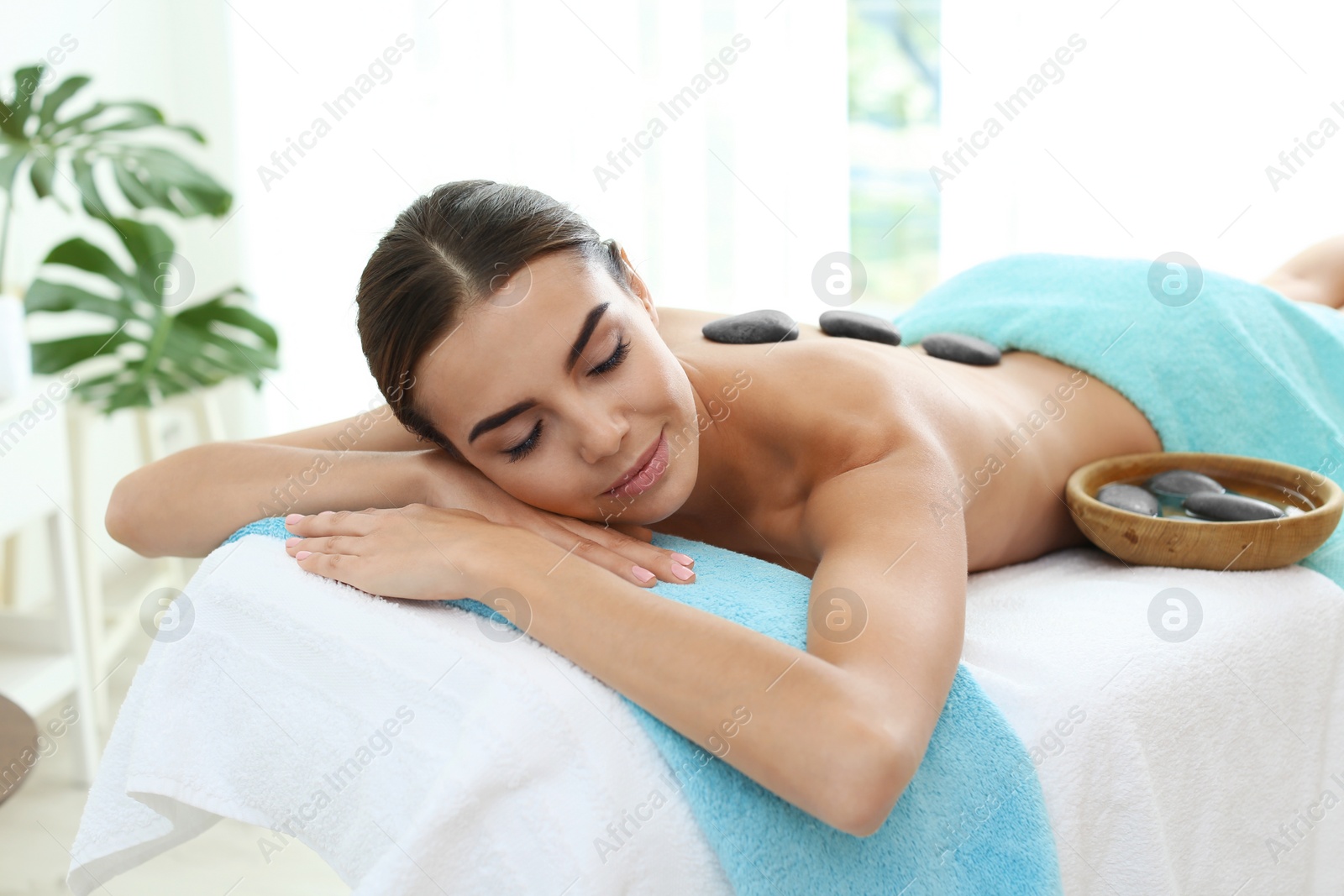 Photo of Beautiful young woman getting hot stone massage in spa salon