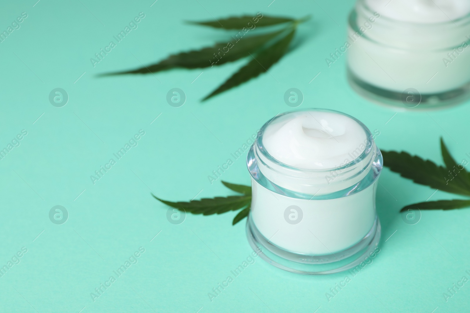 Photo of Glass jar of hemp cream on turquoise background, space for text. Natural cosmetics