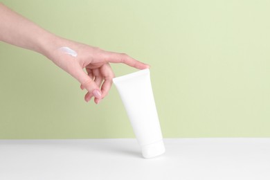 Woman with tube of cream on color background, closeup