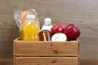 Photo of Humanitarian aid. Different food products for donation in crate on wooden table, closeup