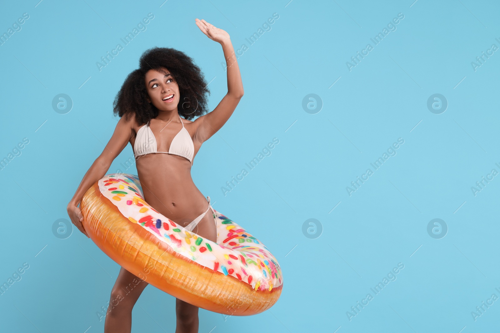 Photo of Beautiful woman in stylish bikini with inflatable ring on light blue background, space for text