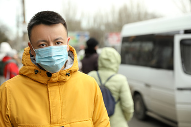 Asian man wearing medical mask on city street, space for text. Virus outbreak