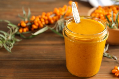 Photo of Delicious sea buckthorn jam and fresh berries on wooden table. Space for text