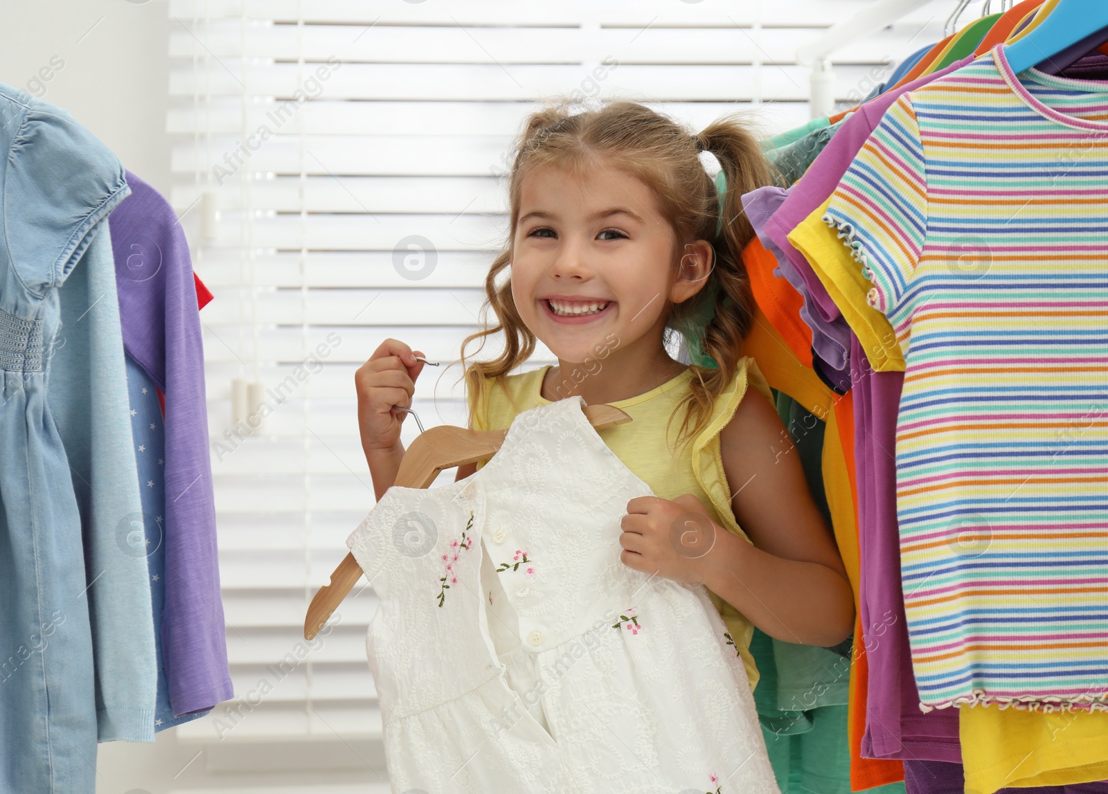 Photo of Little girl choosing clothes on rack indoors