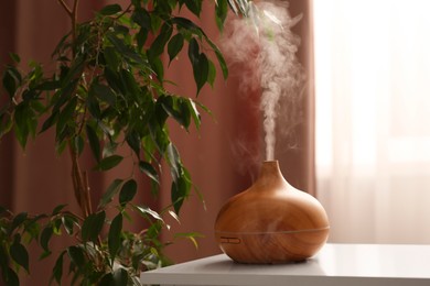 Photo of Air humidifier near houseplant on white table indoors