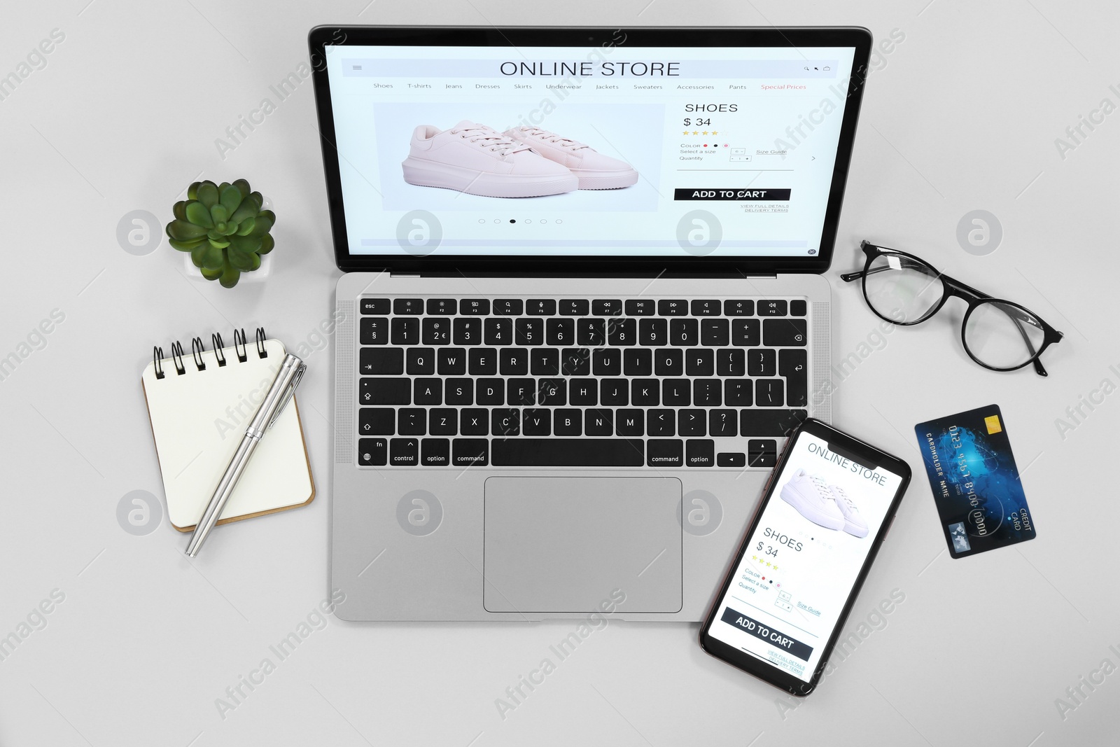 Photo of Online store website on laptop screen. Computer, smartphone, stationery, glasses, credit card and houseplant on grey background, flat lay