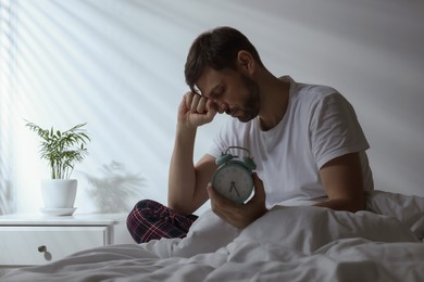 Sleepy man with alarm clock in bed at home