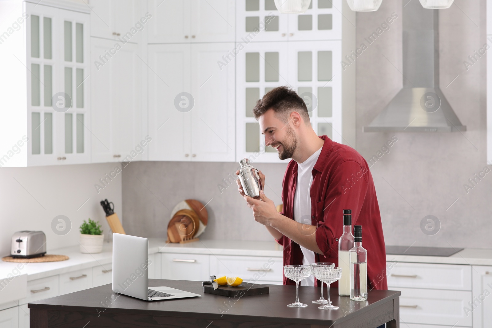 Photo of Man learning to make cocktail with online video on laptop at table in kitchen. Time for hobby