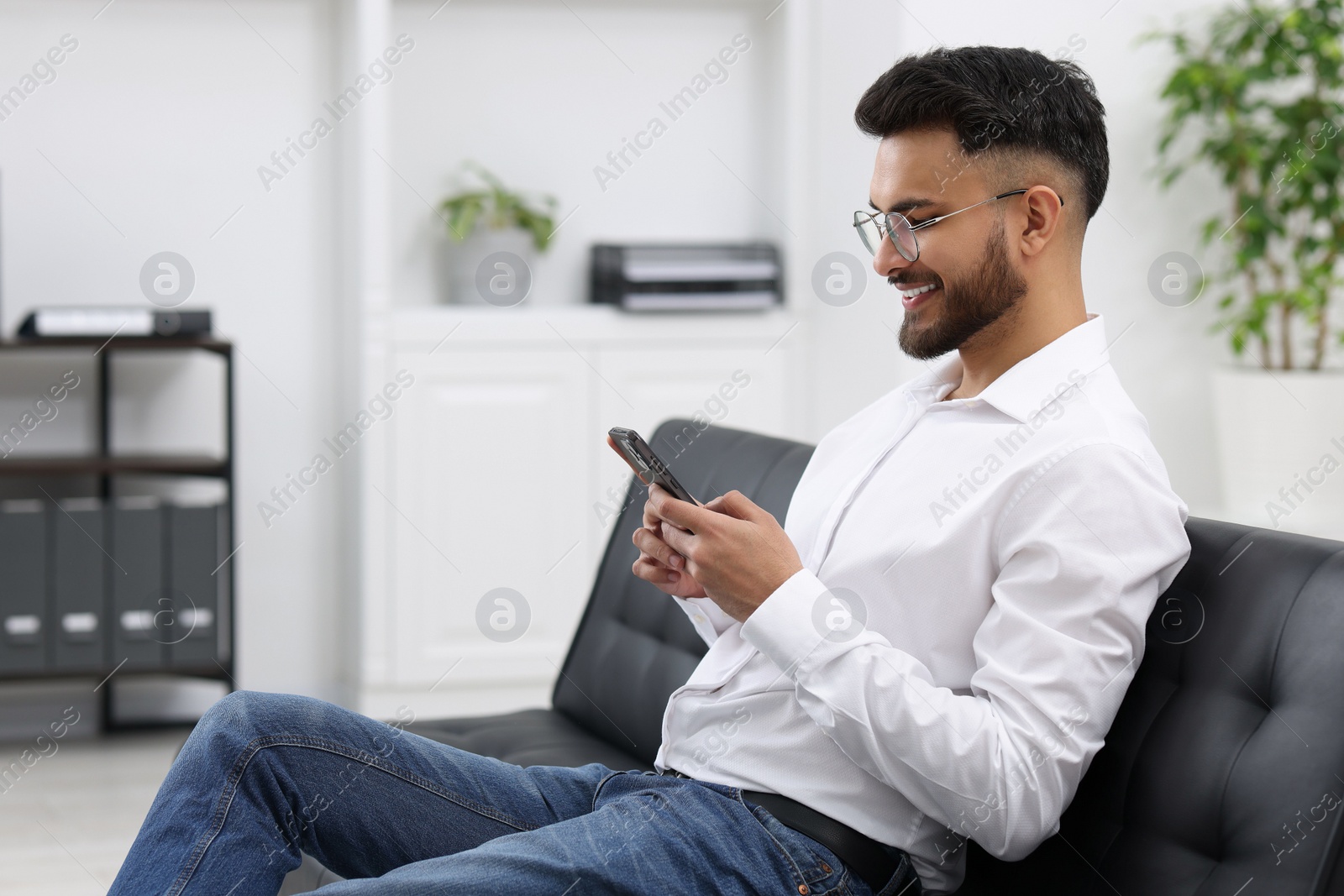 Photo of Handsome young man using smartphone on sofa in office