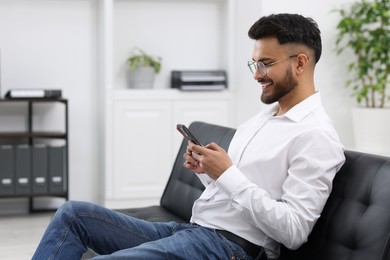 Handsome young man using smartphone on sofa in office