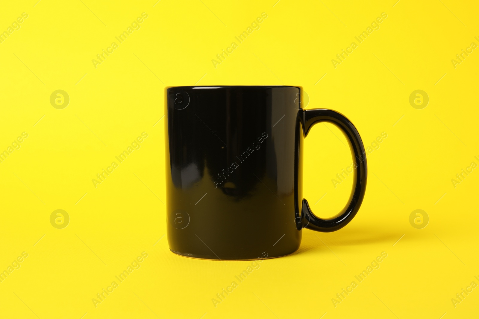 Photo of One black ceramic mug on yellow background