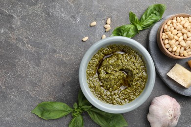 Photo of Tasty pesto sauce in bowl, basil, pine nuts, cheese and garlic on grey table, flat lay. Space for text