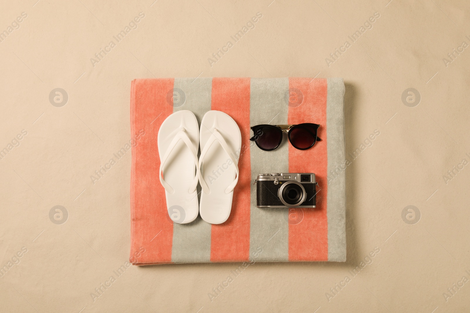 Photo of Beach towel, sunglasses, camera and flip flops on sand, top view