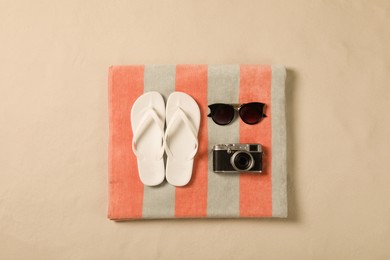 Beach towel, sunglasses, camera and flip flops on sand, top view