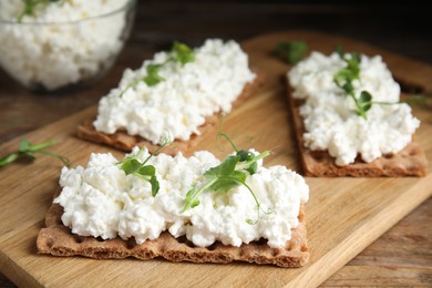 Photo of Crispy crackers with cottage cheese and microgreens on wooden table, closeup