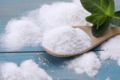Photo of Sweet fructose powder, spoon and mint leaves on light blue wooden table, closeup