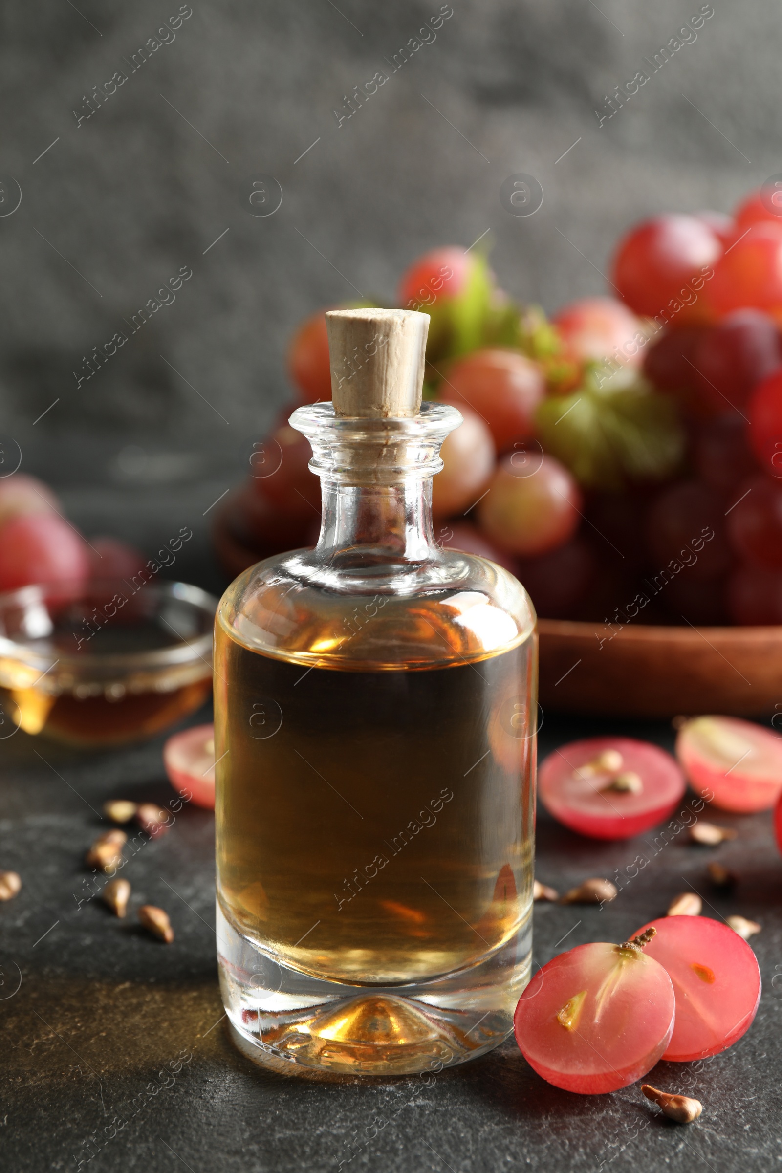 Photo of Organic red grapes, seeds and bottle of natural essential oil on black table