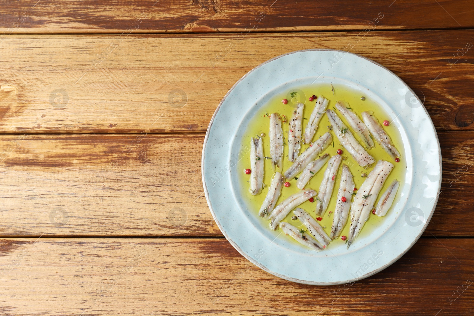 Photo of Tasty pickled anchovies with spices on wooden table, top view. Space for text