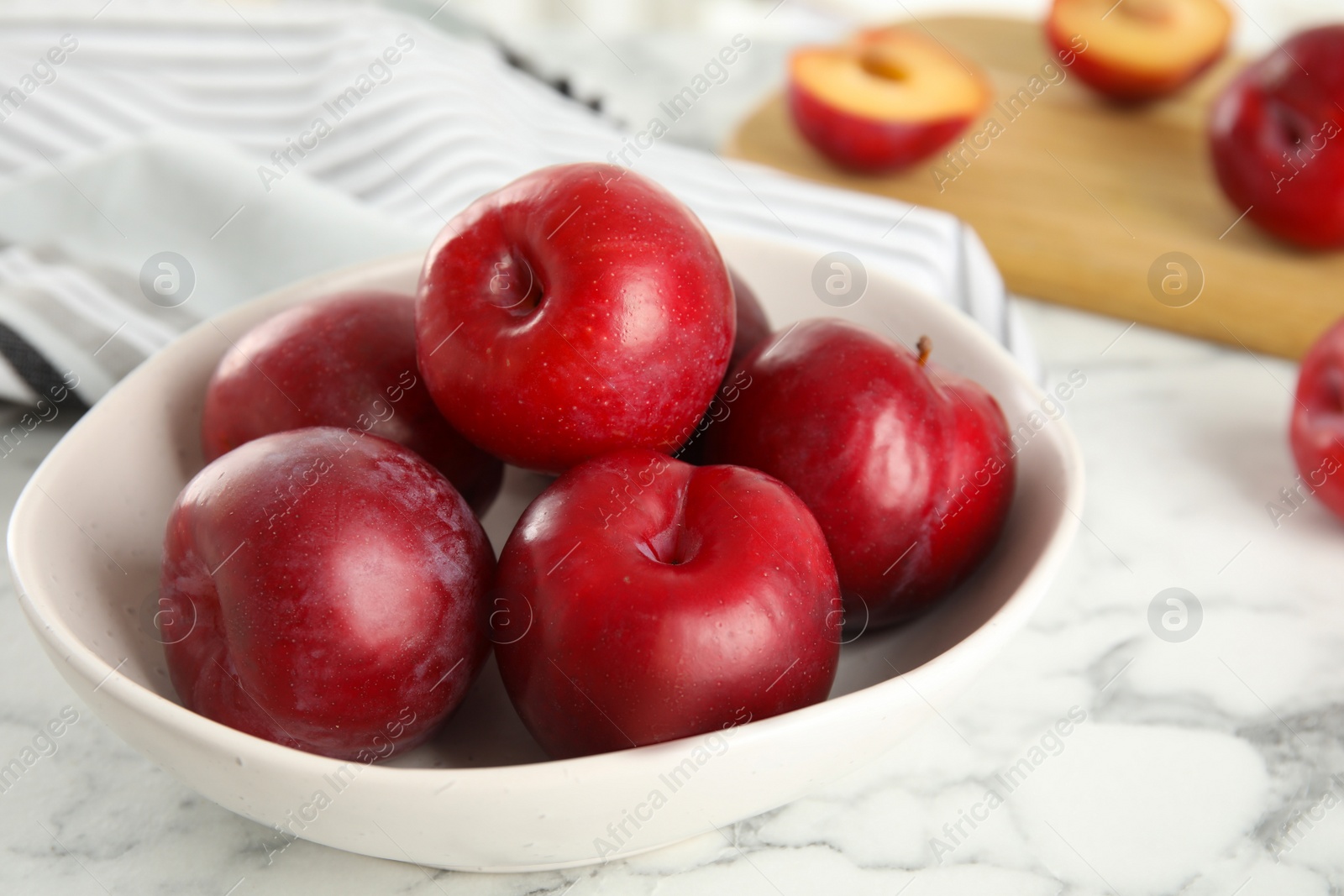 Photo of Delicious ripe plums in bowl on white marble table