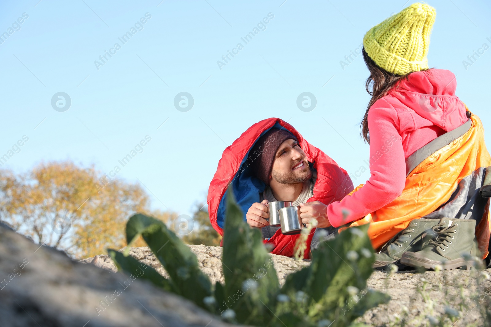 Photo of Couple of campers in sleeping bags sitting on rock. Space for text