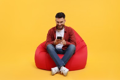 Photo of Happy young man using smartphone on bean bag chair against yellow background