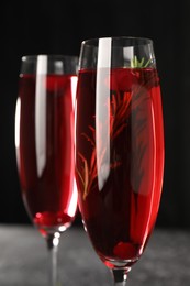 Photo of Tasty cranberry cocktail with rosemary in glasses against dark background, closeup