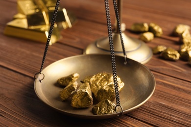 Photo of Scale pan with gold lumps on wooden table, closeup