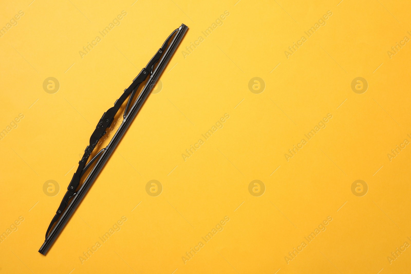Photo of Car windshield wiper on yellow background, top view. Space for text