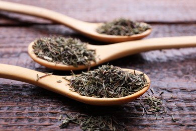 Photo of Spoons with dried thyme on wooden table, closeup