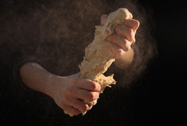 Photo of Making bread. Woman kneading dough on dark background, closeup