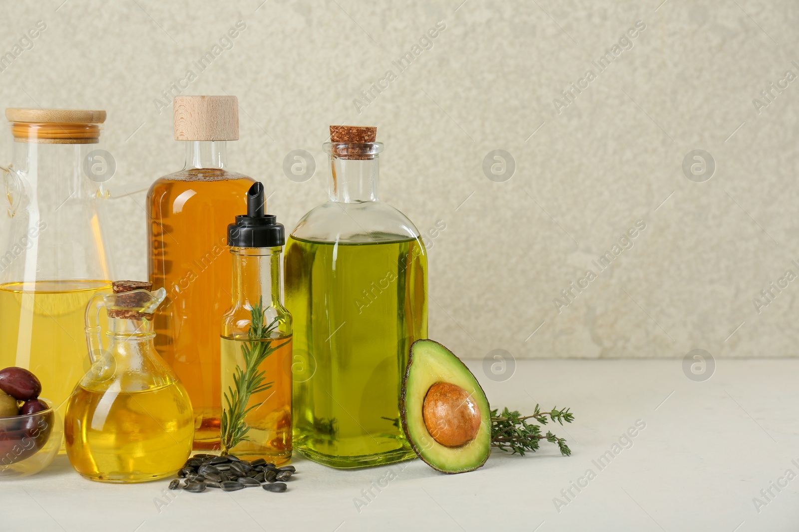 Photo of Vegetable fats. Different cooking oils in glass bottles and ingredients on white table, space for text