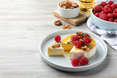 Photo of Brie cheese served with raspberries, walnuts and honey on white wooden table. Space for text