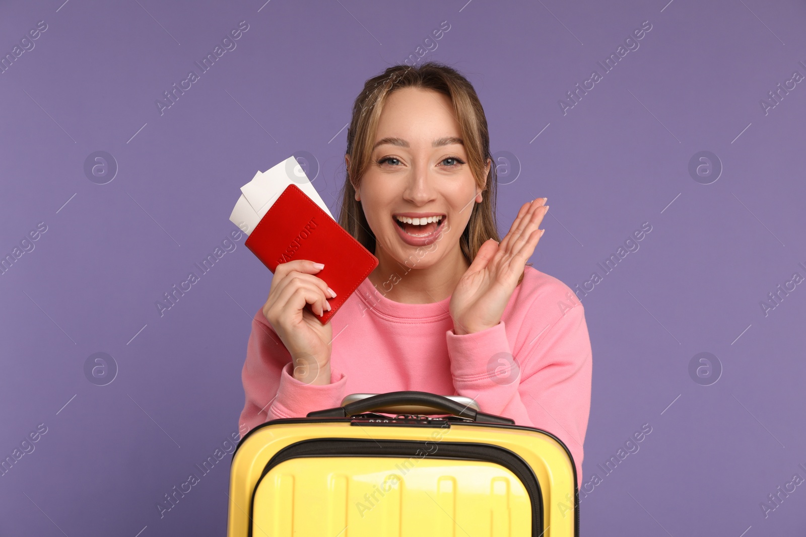 Photo of Happy young woman with passport, ticket and suitcase on purple background