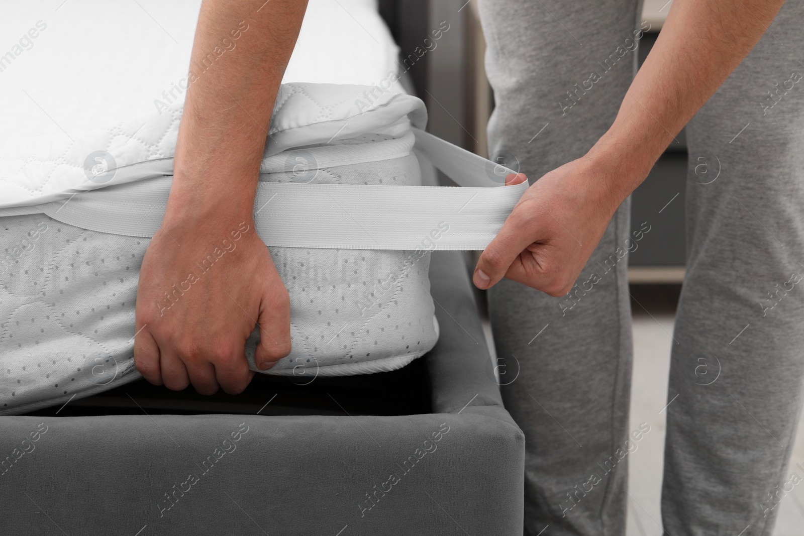 Photo of Man putting protector on mattress indoors, closeup