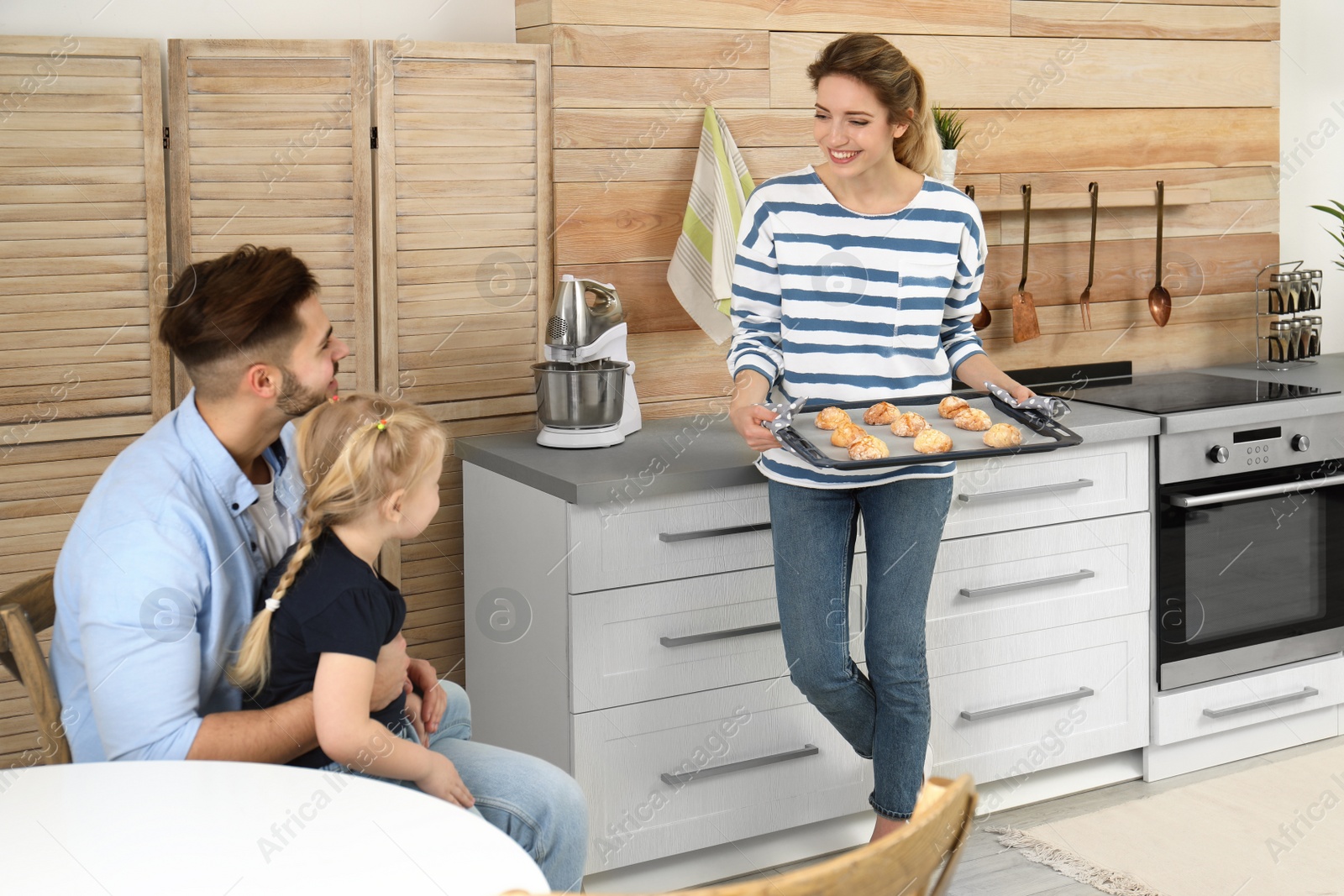 Photo of Young woman treating her family with homemade oven baked cookies in kitchen