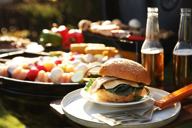 Photo of Tasty burger on table near barbecue grill outdoors. Space for text