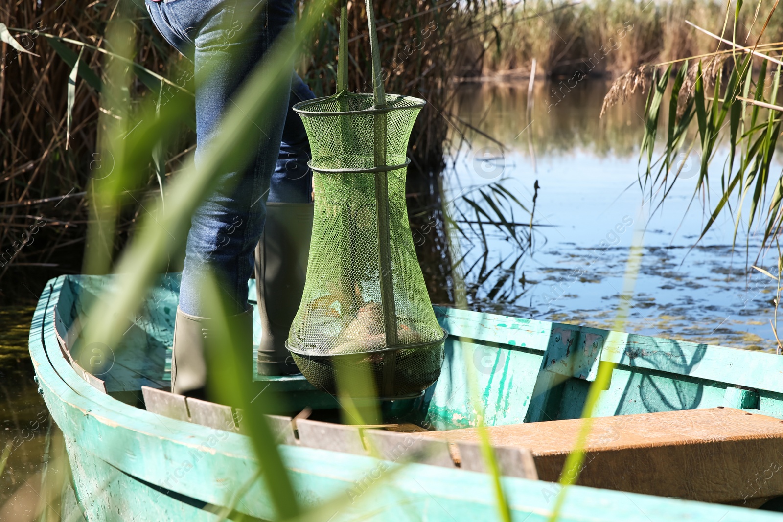 Photo of Man holding fishing net with catch in boat on river