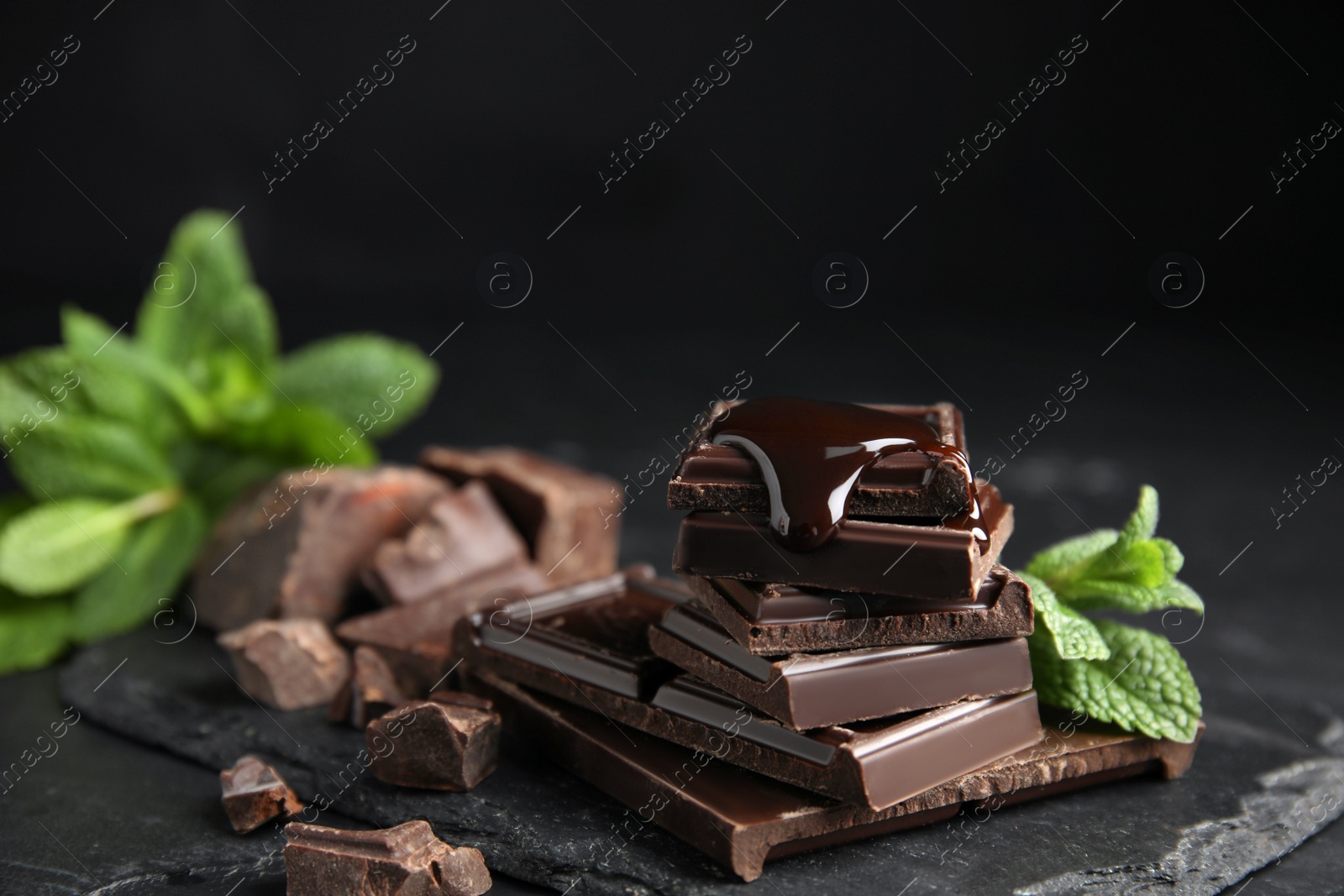 Photo of Tasty chocolate pieces with syrup and mint on black table, closeup