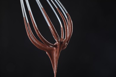 Photo of Chocolate cream flowing from whisk on black background, closeup. Space for text